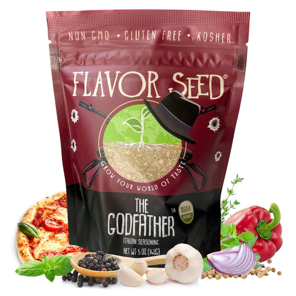 A Flavor Seed The Godfather Italian seasoning pouch on a white background, surrounded by a slice of margherita pizza, fresh basil, a wooden spoon of black peppercorns, garlic, a red bell pepper, half a red onion and sprigs of thyme.