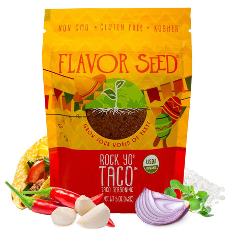 A Flavor Seed Rock Yo' Taco organic taco seasoning pouch on a white background, with a filled taco, red chillies, garlic cloves, half a red onion, fresh oregano and coarse salt around it.