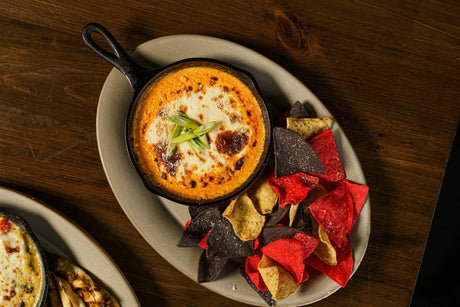 Cast-iron skillet of baked buffalo chicken dip with browned melted cheese and sliced green onion, tortilla chips alongside