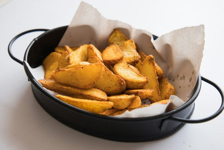 Seasoned potato wedges piled on parchment in a small black round pan on a white surface
