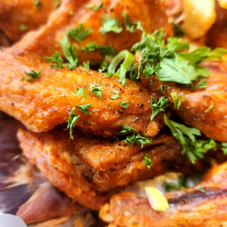Close-up of crisp browned chicken wings dusted with cracked black pepper and scattered with fresh parsley and sliced scallion