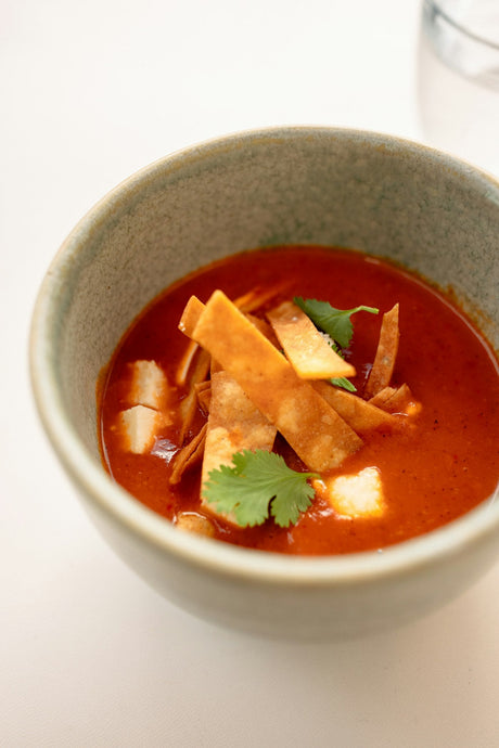 Chicken tortilla soup in a speckled stoneware bowl, topped with crisp fried tortilla strips and fresh cilantro