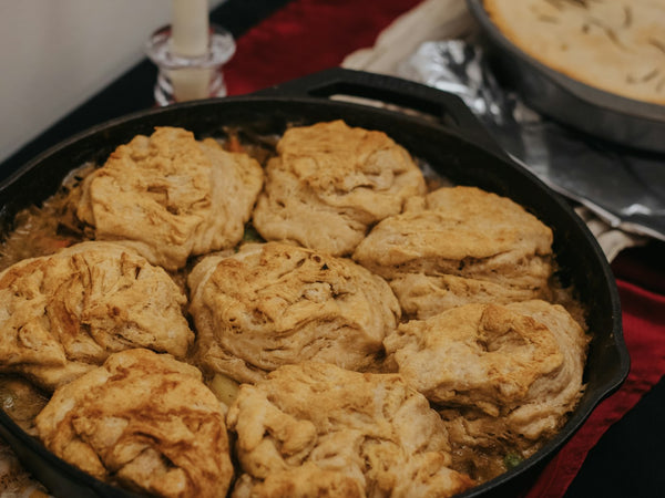 Nine golden-brown biscuits baked on top of a bubbling chicken filling in a black cast iron skillet, with carrot and peas showing around the rim.